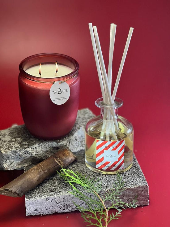 Rouge Candle and Reed Diffuser set from the Rouge Collection on a red background, featuring a lit candle and aromatic reed diffuser.